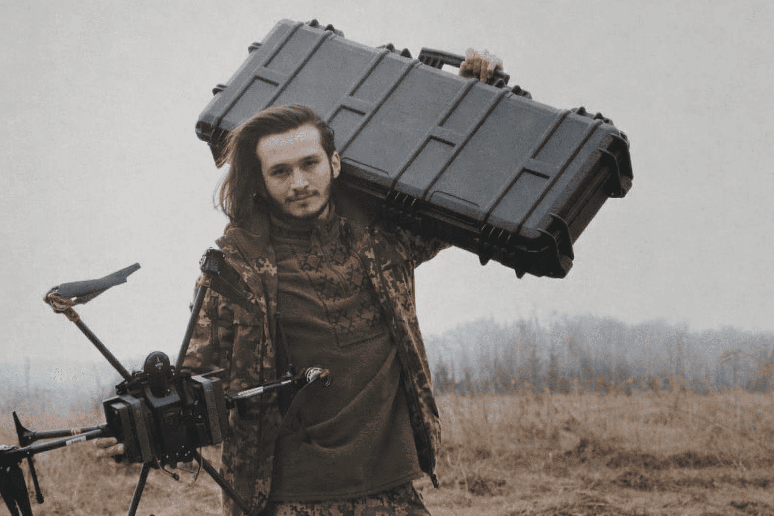 Олексій Бабенко, CEO Vyriy Industries, переносить обладнання для дронів на тлі польового майданчика.